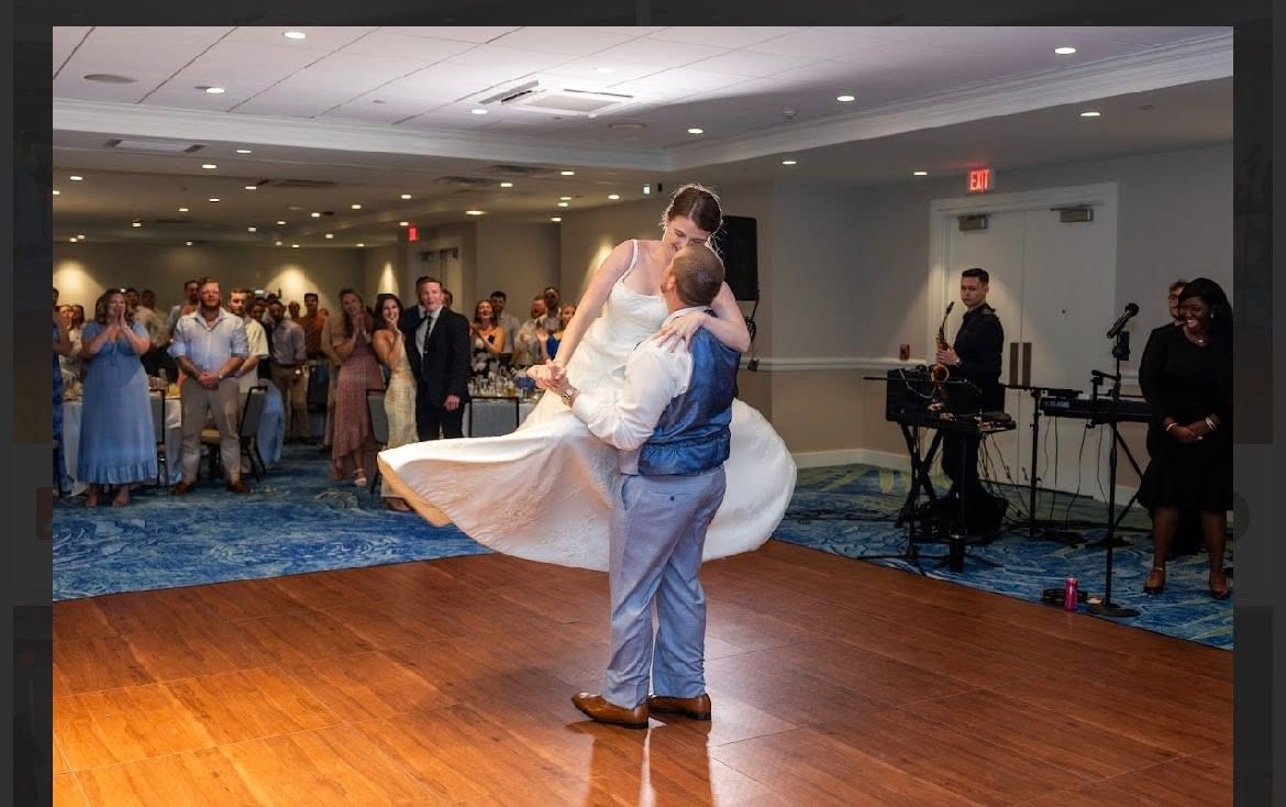 Groom lifting his bride on a wooden reception dance floor as guests applaud