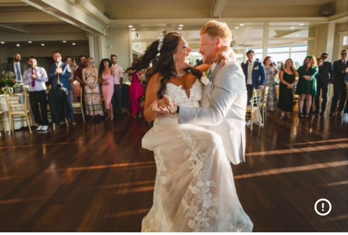 Newlyweds smiling at each other during a lift and spin on a sunlit dance floor