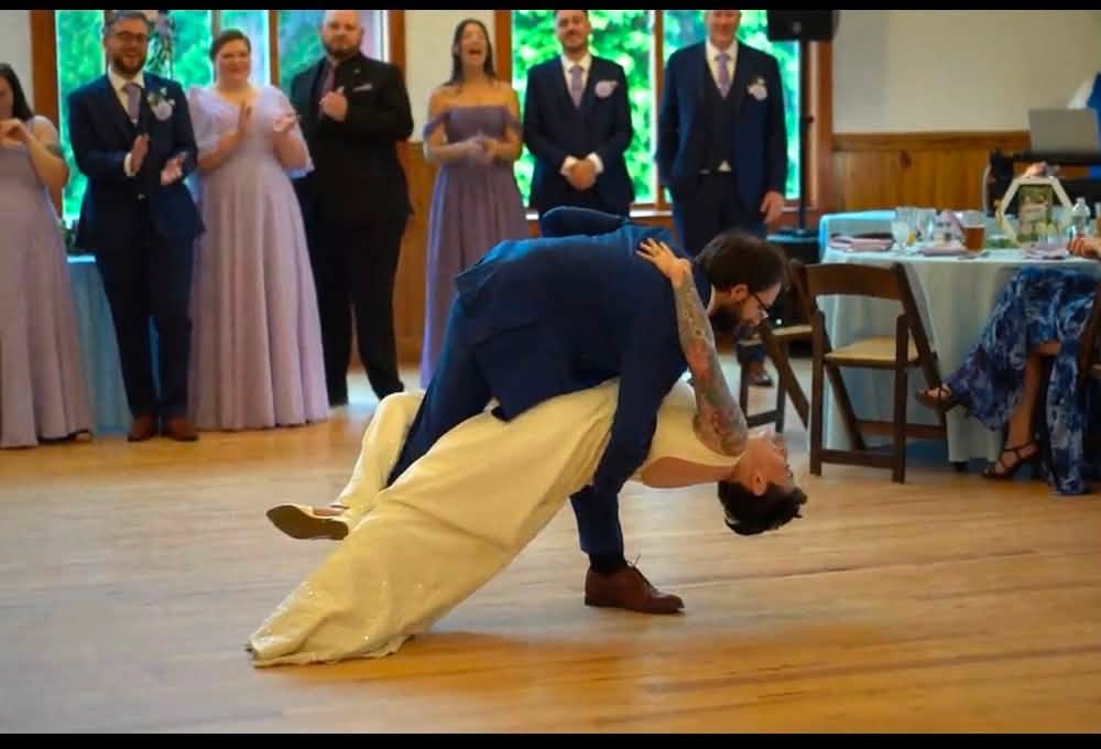 Groom in a navy suit dipping his bride in front of their wedding party