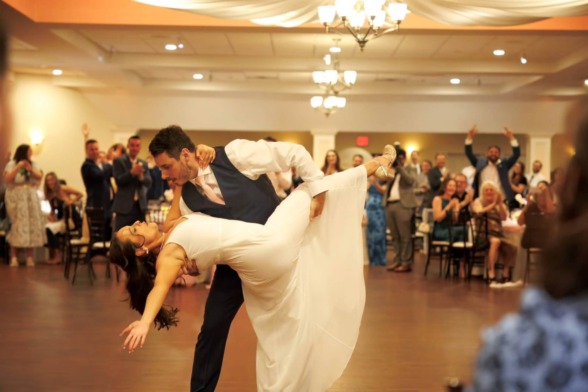 Bride extending her arm during a dramatic dip as wedding guests cheer