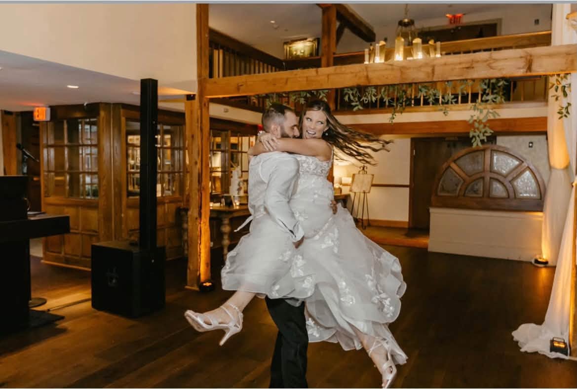 Groom lifting his smiling bride during their first dance in a timber-framed venue